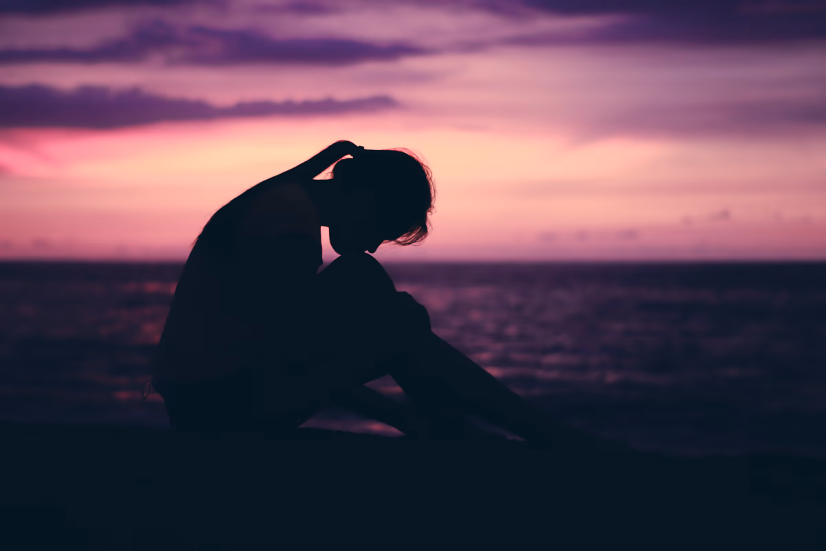 Contemplative silhouette seated on a beach during a purple and magenta twilight