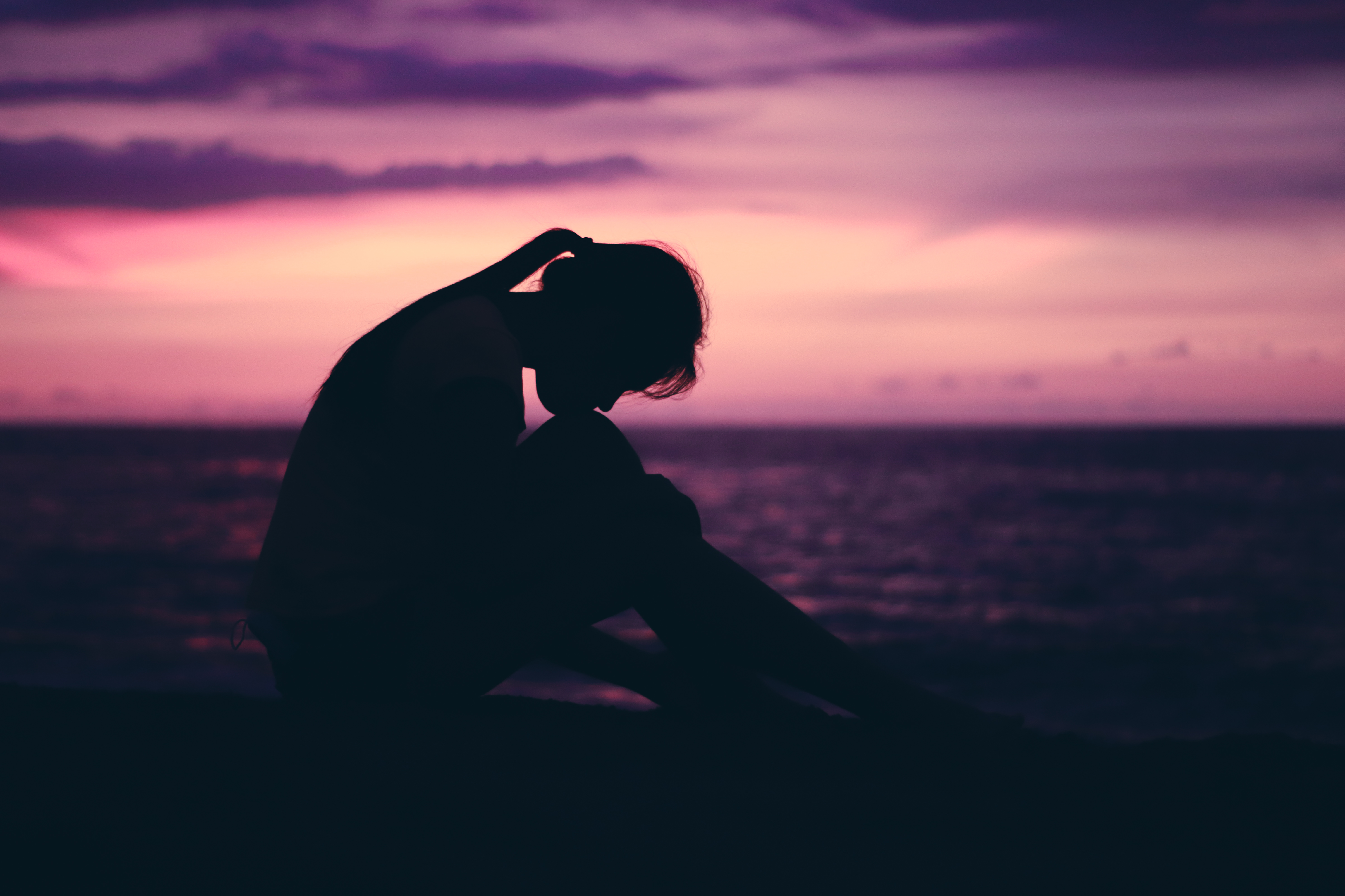 Contemplative silhouette seated on a beach during a purple and magenta twilight