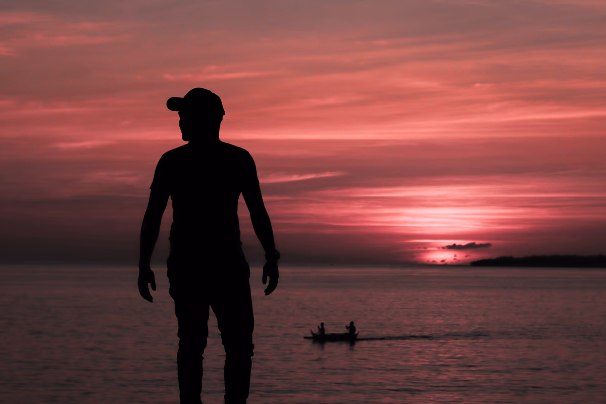 Silhouetted figure watching a vibrant pink sunset over calm water with a distant