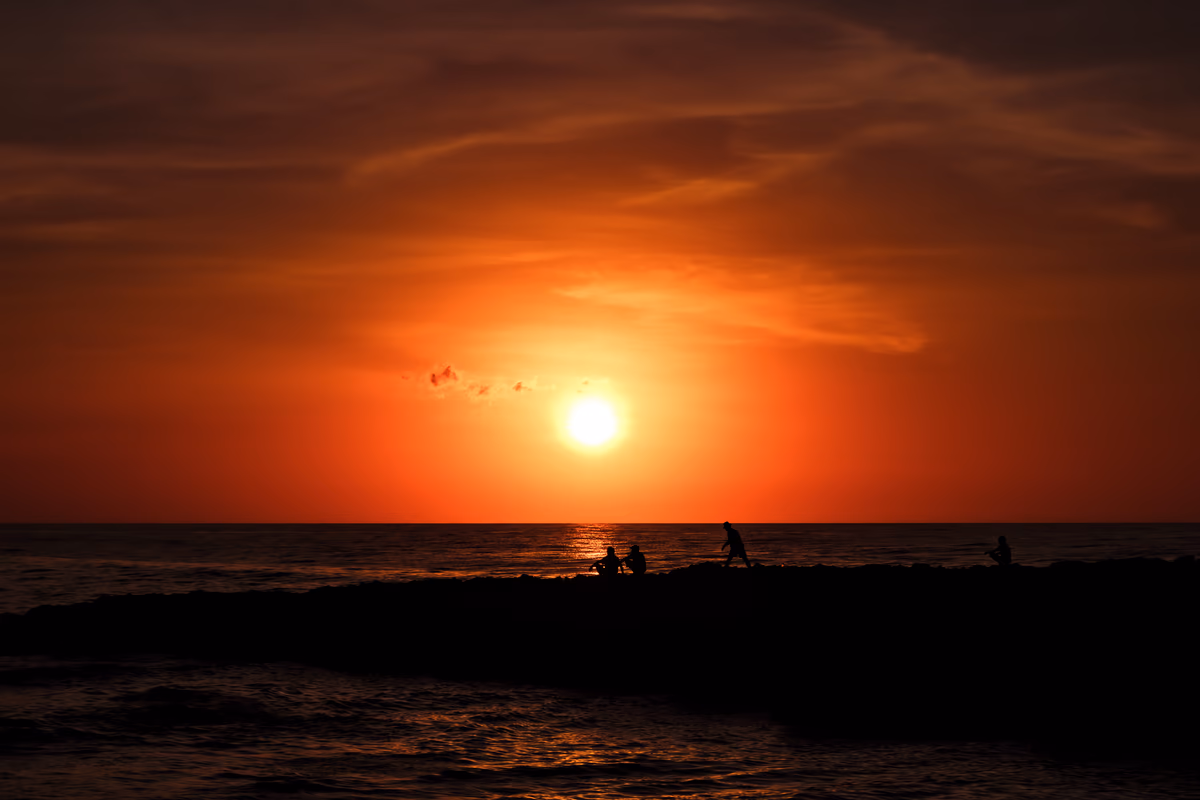 Dramatic orange sunset over the ocean with silhouetted figures on a rocky shorel