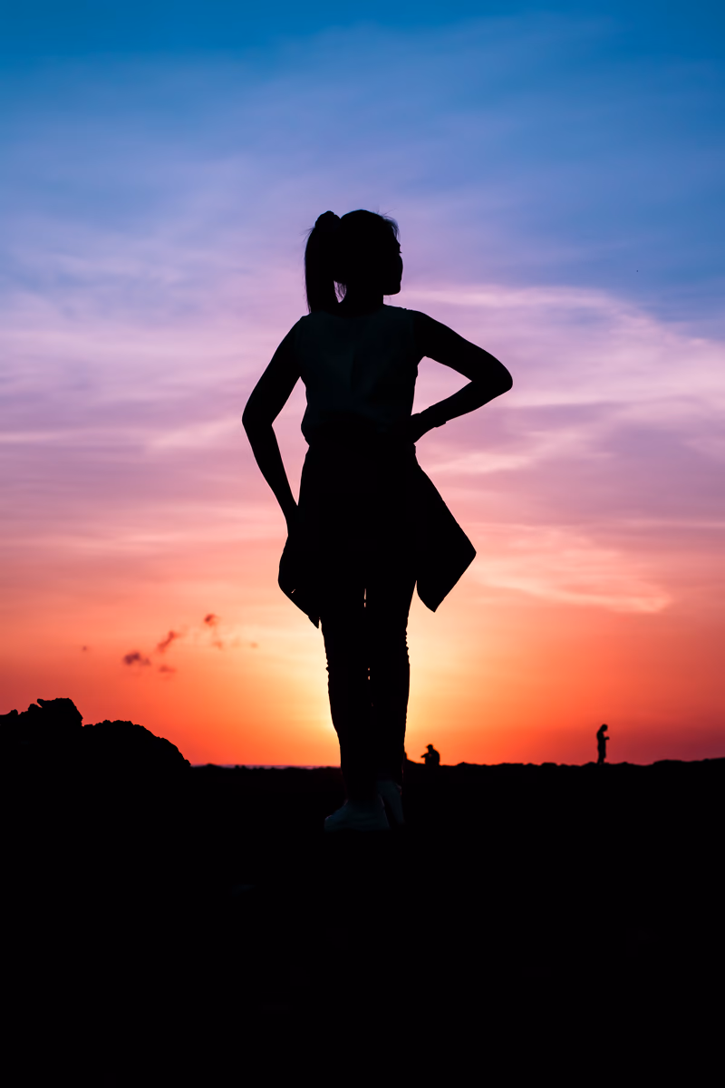 Confident silhouette with hands on hips facing a fiery orange and purple sunset