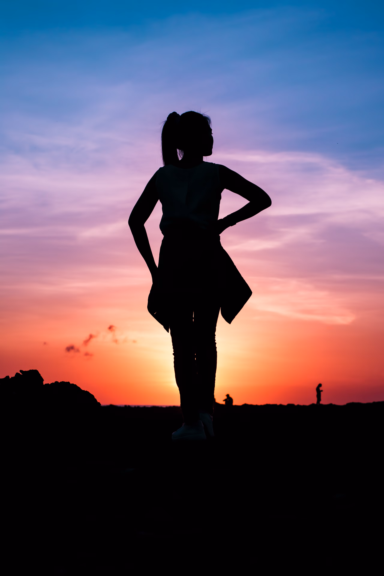 Confident silhouette with hands on hips facing a fiery orange and purple sunset