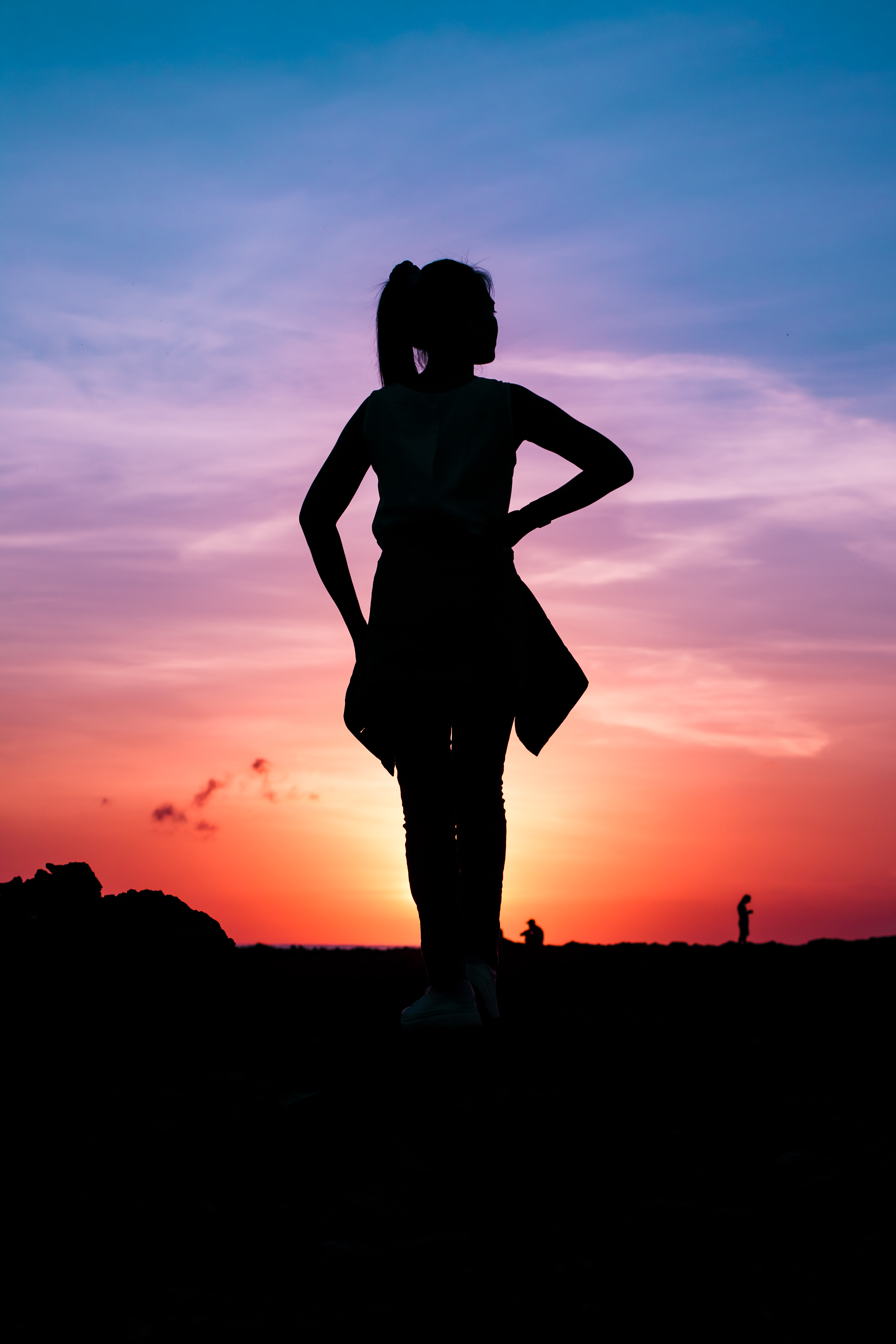 Confident silhouette with hands on hips facing a fiery orange and purple sunset