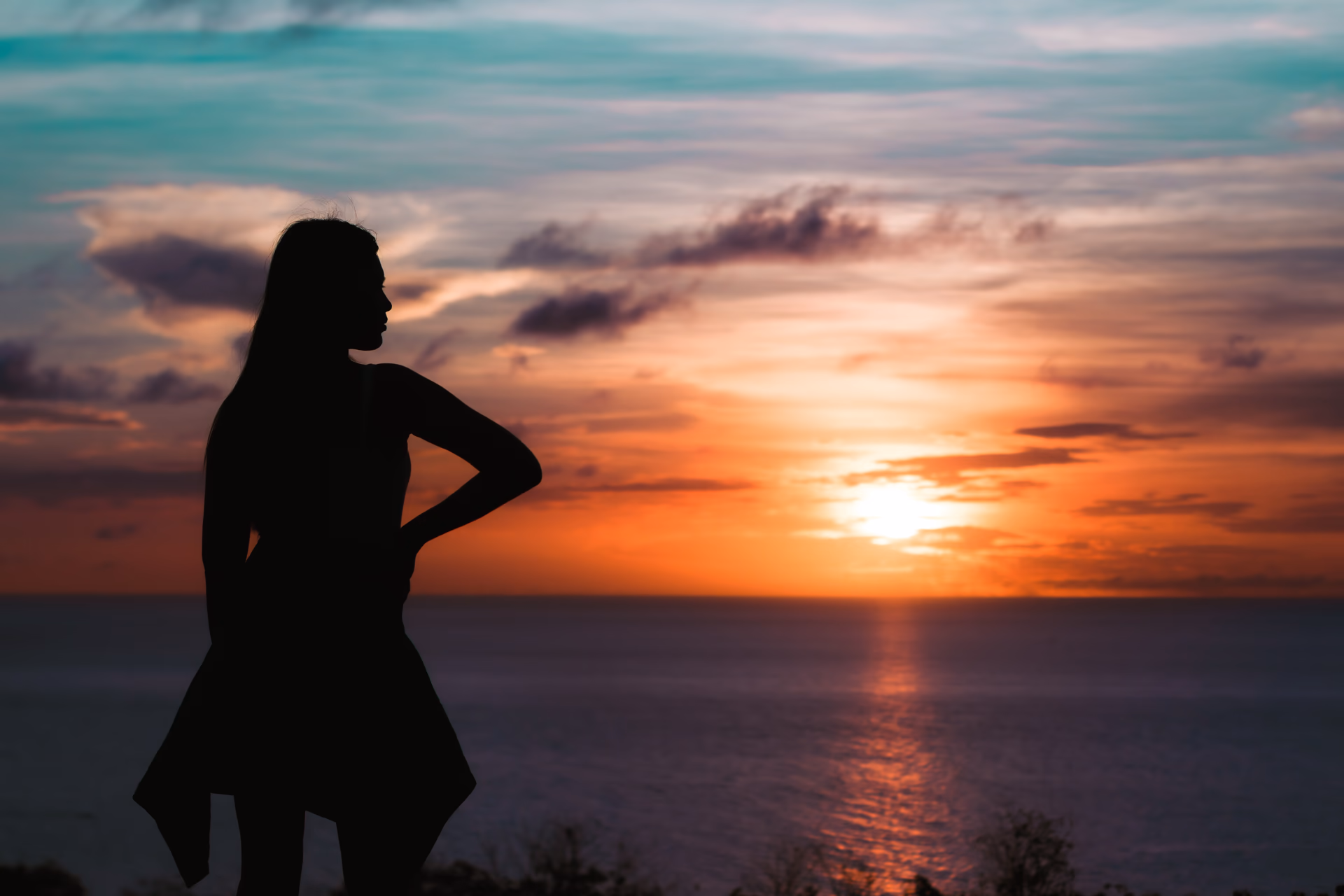 Silhouetted figure overlooking a teal and orange sunset over the ocean