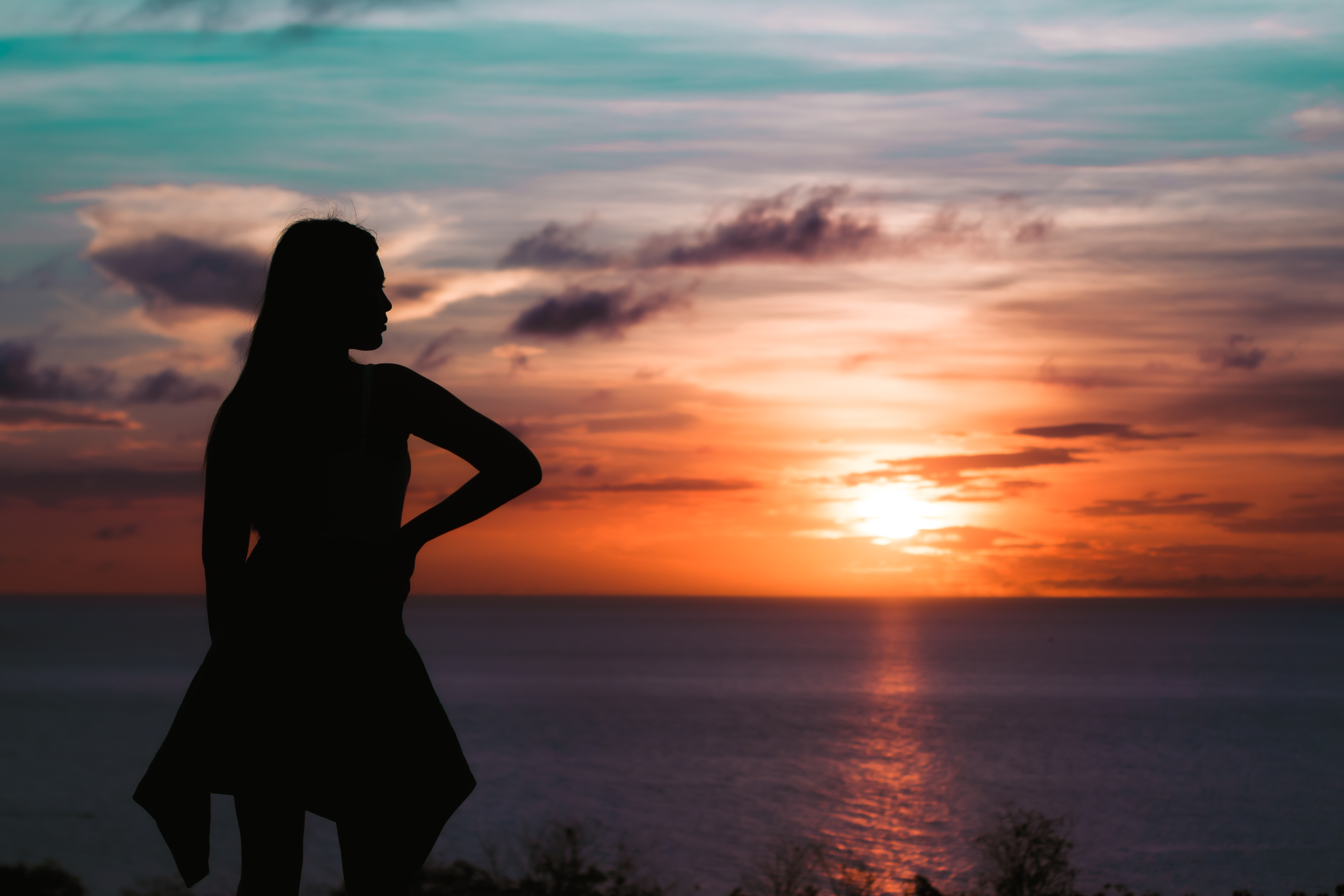 Silhouetted figure overlooking a teal and orange sunset over the ocean
