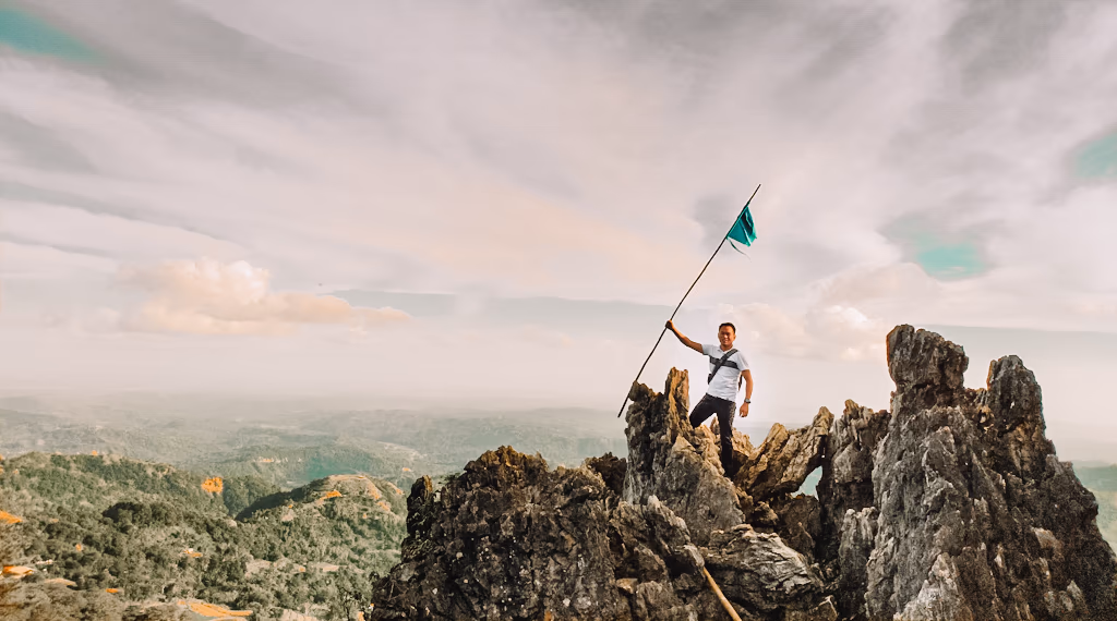 Adventurer standing on a jagged mountain peak holding a flag above misty valleys